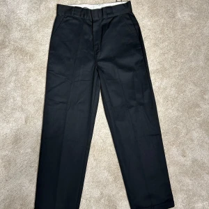 Dickies - Snygga svarta byxor från Dickies med en klassisk design. Byxorna har en rak passform och är tillverkade i ett slitstarkt material. Perfekta för en stilren look.