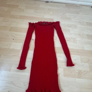 Röd ribbad klänning från FB Sister - Snygg röd ribbad klänning från FB Sister med offshoulder-design och långa ärmar. Perfekt för att sticka ut med sin livfulla färg och stiliga passform. Klänningen har en volangdetalj vid halsen som ger en extra touch av elegans.