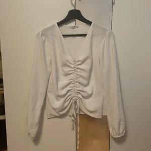 Vit blus från Hailys - Säljer en vit söt blus från Hailys med v-ringning och snygg knytning framtill. Blusen har långa ärmar och en lätt textur i tyget. Har inga defekter.