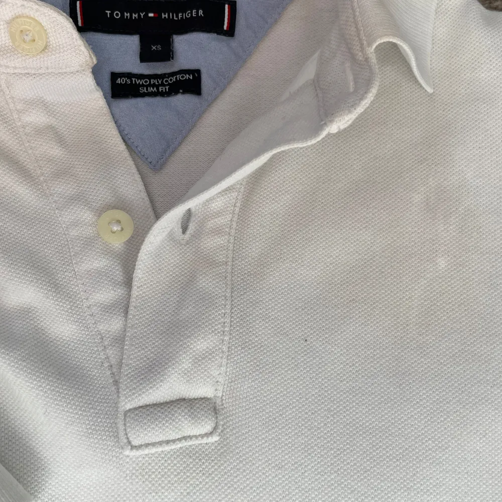 Säljer en stilren vit pikétröja från Tommy Hilfiger i storlek XS. Tröjan har korta ärmar och en klassisk krage med knappar. Den är tillverkad i bomull och har en liten logotyp på bröstet. Perfekt för en avslappnad och snygg look.. Neuletakit & Villapaidat.