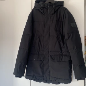 Svart dunjacka från McKinley parkas - Säljer en svart dunjacka från McKinley , parkas med huva och långa ärmar. Jackan har en stilren design med dragkedja och praktiska fickor framtill. Perfekt för kyliga dagar.