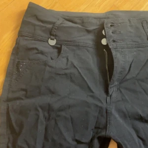 Svarta byxor med detaljer - Snygga svarta byxor Byxorna har dekorativa detaljer på bakfickorna och fram framfickorna som ger en extra touch. Perfekta för en stilren look. 