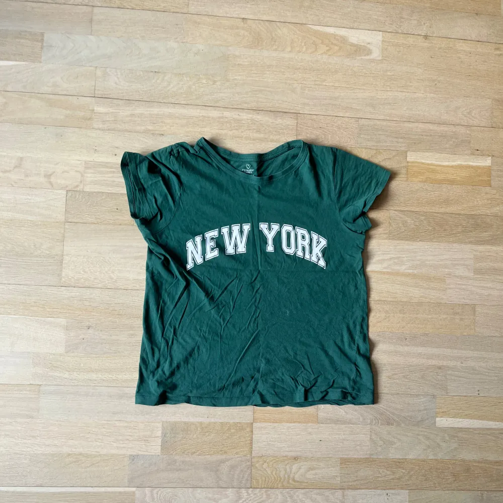 Säljer en grön t-shirt med texten 'New York' i vitt på framsidan. T-shirten har korta ärmar och en avslappnad passform. Perfekt för en casual look.. T-paidat.