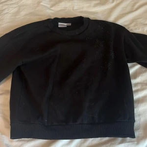 Svart tröja med paljettdetaljer - Säljer en svart tröja med paljettdetaljer på framsidan. Tröjan har långa ärmar och ribbade muddar vid ärmslut och nederkant. Perfekt för en stilren look.