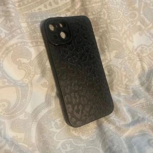 Leopardmönstrat mobilskal - Snyggt svart mobilskal med diskret leopardmönster. Skalet har en slät yta och är designat för att skydda din telefon samtidigt som det ger en stilren look. Perfekt för dig som vill ha ett djuriskt inslag i din vardag. iPhone 13/14
