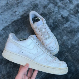 Vita Nike Air Force sneakers - Säljer ett par klassiska vita Nike Air Force sneakers. De har en stilren design med snörning och perforerade detaljer på tån för ventilation. Perfekta för en casual look.