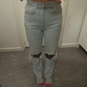 Ljusa jeans med slitna knän - Snygga ljusa jeans med slitna knän och hög midja. Perfekta för en avslappnad stil. Klassisk femficksdesign med knapp och dragkedja framtill.