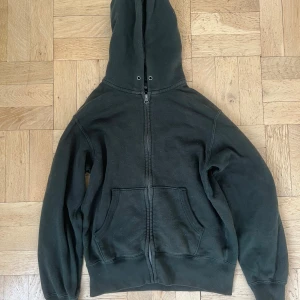 Mörkgrön hoodie från Uniqlo - Säljer en mörkgrön hoodie från Uniqlo med dragkedja och fickor framtill. Perfekt för en avslappnad stil. Den har en klassisk design med huva och långa ärmar.