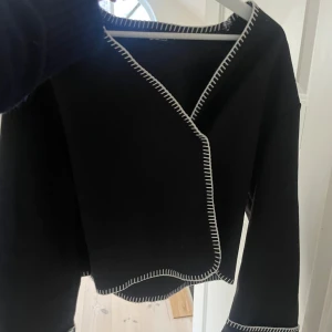 Svart tröja - Svart omlottopp från Gina med vita sömmar 