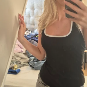 Svart halterneck topp med vit kant - Svart halterneck topp med en vit kant. Går att justera i nacken med snören. Öppen rygg. Köpare står för frakt