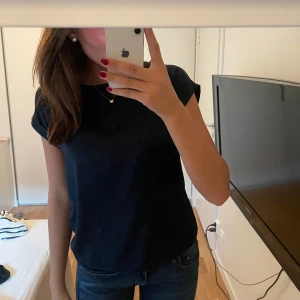 Mörkblå satinblus - Säljer en elegant mörkblå blus i satinmaterial. Den har en enkel och stilren design med korta ärmar. Perfekt för både vardag och fest!