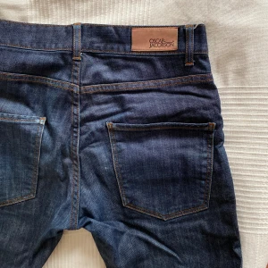 Oscar Jacsobson jeans - Mörkblåa jeans med slim fit passform. Säljer då jag växt ut dem. Använda men i bra skick. Lite synliga skitmarkeringar från mobilen i fickan och en liten ljus fläck på ena benet. S  Skriv vid frågor!
