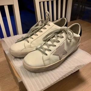 Golden Goose vita sneakers med grå stjärna - Säljer ett par feta Golden Goose skor i storlek 42!! Inga defekter och är i gott skick då dom bara är använda ca 5 gånger!! Stl 42 men passar även mig som har 43!! Box får man med vid köpet!! Pris kan diskuteras!!