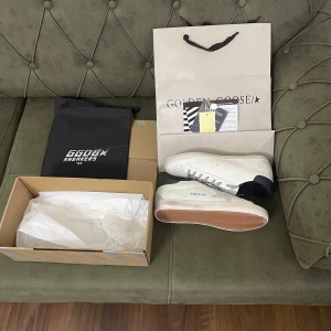 Vita sneakers från Golden Goose - Snygga vita sneakers från Golden Goose med svarta detaljer och en stjärna på sidan. Skorna har en klassisk snörning och en gummisula med fiskbensmönster. Perfekta för en stilren look. Skorna är helt äkta för bara 2199