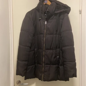 Svart dunjacka från Vero Moda - Säljer en svart dunjacka från Vero Moda med dragkedja och huva. Jackan har långa ärmar och är perfekt för kalla dagar. Den har en stilren design med quiltade detaljer och dragsko vid huvan.