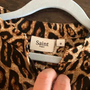Leopardmönstrad klänning från Saint Tropez - Snygg leopardmönstrad klänning från Saint Tropez i storlek M. Klänningen har långa ärmar och ett bälte i midjan för en smickrande passform. Perfekt för att sticka ut med ett djärvt mönster.