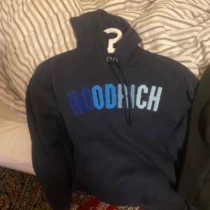 Mörkblå hoodie från Hoodrich - Säljer en mörkblå hoodie från Hoodrich med texten 'HOODRICH' i olika blå nyanser på bröstet. Den har en justerbar huva med dragsko och en stor magficka. Perfekt för en avslappnad stil. Den är i bra skick skriv om ni har några funderingar 