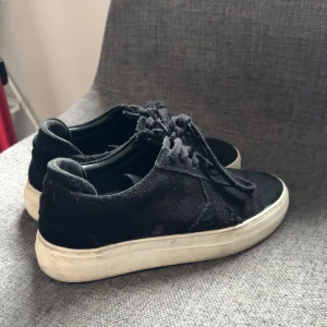 Svarta sneakers från Axel Arigato - Snygga svarta sneakers i mocka från Axel Arigato med vit sula. Skorna har klassisk snörning och en stilren design som passar perfekt till vardags. Märket är synligt på sulan.