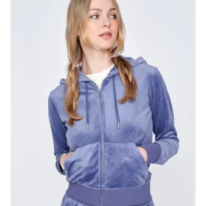 Juicy couture zip up - Säljer en snygg blå velourjacka från Juicy Couture. Jackan har en dragkedja framtill och en huva med knytband. Perfekt för en avslappnad stil med ribbade muddar vid ärmslut och nederkant.