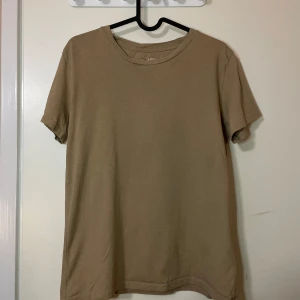Beige t-shirt från 157 - Säljer en enkel och stilren beige t-shirt från 157 i storlek M. T-shirten är tillverkad av 100% bomull och har en klassisk rund halsringning. Perfekt för en avslappnad look.