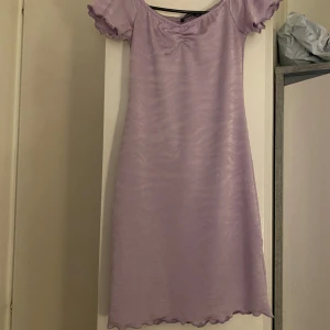 Ljuslila klänning från Busem - Säljer en söt ljuslila klänning från Busem med korta ärmar och en subtil rynkdetalj vid halsen. Klänningen har en vågig textur och en avslappnad passform som ger en romantisk känsla. Perfekt för vårens och sommarens varma dagar. 🌸