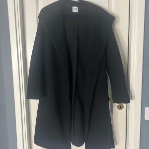 Svart kappa från Zara - Snygg svart kappa från Zara med huva. Perfekt för kyligare dagar. Den har en stilren design och är långärmad, vilket gör den både praktisk och trendig.