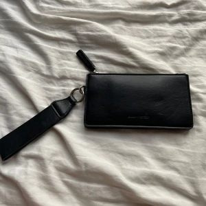 Svart plånbok från Carin Wester - Snygg svart plånbok från Carin Wester i skinn. Den har en praktisk dragkedja och flera fack för kort och kontanter. Perfekt för att hålla ordning på dina värdesaker med stil.