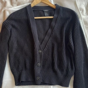 Super fin svart stickad kofta  - Säljer en svart stickad kofta från Lindex med knappar framtill. Koftan har en djup v-ringning och ribbade muddar vid ärmslut och nederkant. Är inte lika tjock i materialet som mycket annat stickat så den sitter super fint på kroppen