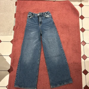 Blå jeansbyxor med vida ben - Snygga blå jeansbyxor med vida ben och hög midja. Klassisk femficksdesign med knapp och dragkedja framtill. Perfekta för en avslappnad stil.