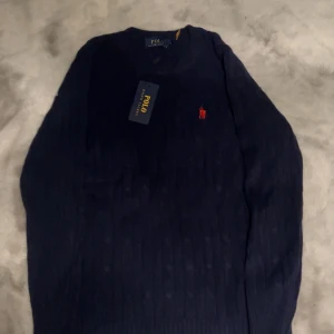 Mörkblå tröja från Ralph Lauren - Säljer en stilren mörkblå tröja från Ralph Lauren med det klassiska röda logotypbroderiet på bröstet. Tröjan har en rund halsringning och är perfekt för en elegant vardagslook. Passar utmärkt till både jeans och chinos. Storlek s 