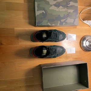 Valentino Rockrunner sneakers - Snygga Valentino Rockrunner sneakers i en cool camouflage-design. Skorna har en kombination av skinn och mocka med färgdetaljer i turkos och orange. De har en robust sula och klassisk snörning. Perfekta för en stilren look. Priset kan diskuteras!!!!! Köpta för 8500kr obs ! Ska rengöra de om du vill de!!!