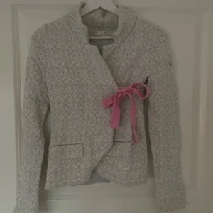 Grå mönstrad kofta med rosa detaljer - Säljer en elegant grå kofta från oss molly med ett subtilt mönster och rosa rosett framtill. Jätte fint skick (nästan aldrig använd), storlek 0, skulle säga motsvarar en xs-s🥰