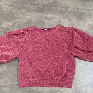 Rosa glittrig topp från Bik Bok - Säljer en rosa glittrig topp från Bik Bok med puffiga ärmar och rund halsringning. Perfekt för att lysa upp vilken outfit som helst. Toppen har en elastisk nederkant för en bekväm passform. Passar perfekt för festliga tillfällen! ✨