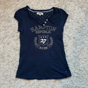 Marinblå t-shirt från Hampton Republic - Säljer en marinblå t-shirt från Hampton Republic med tryck framtill. T-shirten har en rund halsringning med knappar och korta ärmar. Skriv för fler frågor eller funderingar💕