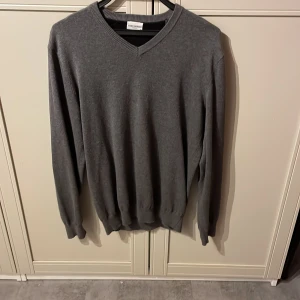 Grå tröja från John Henric - Säljer en stilren grå tröja från John Henric med v-ringning och svarta armbågslappar. Perfekt för en klassisk look. Tröjan har långa ärmar och ribbade muddar vid ärmslut och nederkant. Riktigt skönt material