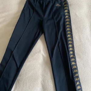 Svarta byxor från Kappa - Svarta byxor från Kappa med gulddetaljer. Storlek xs och passar mig som är 173.