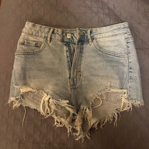 Blå jeansshorts från Zara - Säljer ett par snygga blå jeansshorts från Zara med slitna detaljer och fransiga kanter. Shortsen har en hög midja och klassisk femficksdesign. Perfekta för en sommarkväll 💗