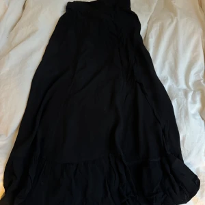 Svart långkjol från H&M - Snygg svart långkjol från H&M i en flowy design. Kjolen har en elastisk midja för extra komfort och en subtil volangdetalj längst ner. Perfekt för att skapa en elegant look.