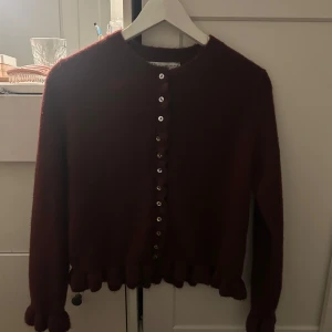 Vinröd kofta från Zara - Säljer en vinröd kofta från Zara med knappar framtill. Koftan har långa ärmar och en fin volangdetalj vid nederkanten. Storlek S och nyskick
