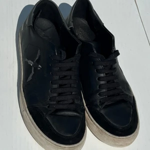 Svarta sneakers med snörning - Snygga svarta sneakers med snörning och en vit sula. Skorna har en diskret logga på sidan och är perfekta för en avslappnad stil. inte jättebra skick men fortfarande väldigt snygga och otroligt sköna. Dustbag och låda följer med hör av er vid frågor 