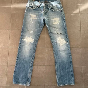 Blå dondup jeans George - Säljer ett par blå jeans med slitna detaljer och hål för en trendig look. De har en klassisk femficksdesign och knappgylf. Perfekta för en avslappnad stil.
