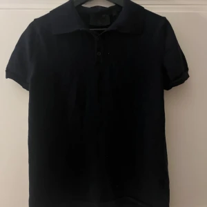 Marinblå pikétröja från Dahlin - Snygg marinblå pikétröja från Dahlin med klassisk krage och knappar framtill. Perfekt för en stilren look. Kortärmad design som passar bra till både jeans och chinos. Utmärkt skick utan tecken på användning och väldigt skönt material!