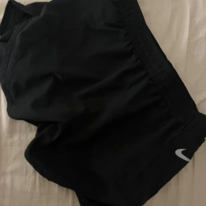 Svarta träningsshorts från Nike - Snygga svarta träningsshorts från Nike med elastisk midja och en liten logga på benet. Perfekta för en aktiv livsstil och bekväma att bära under träning.