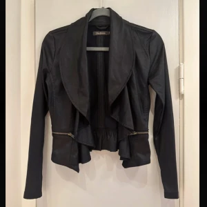 Svart jacka från Alice Bizous - Snygg svart jacka från Alice Bizous i storlek XS. Jackan har en cool design med dragkedjedetaljer och en unik skärning framtill. Tillverkad i 100% polyester, perfekt för en stilren look.