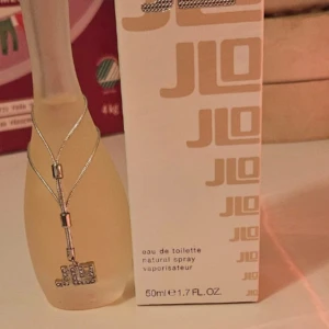 Parfym Glow by JLo - Säljer en elegant parfymflaska från JLo, Glow, med en volym på 50 ml. Flaskan har en mjuk, frostad yta och är dekorerad med ett silverfärgat halsband. Doften är en eau de toilette, perfekt för en fräsch och lätt känsla.