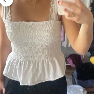 Vit smockad linnetopp med spetsdetaljer - Säljer en söt vit linnetopp med smockad design och spetsdetaljer vid axelbanden. Toppen har en luftig passform och är perfekt för varma dagar.                                       Är i storlek L men PASSAR FOLK SOM HAR XS/S/M som mig !!!💞