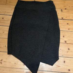 Snygg grå kjol från Gina Tricot i en asymmetrisk design. Kjolen har en dragkedja baktill och är tillverkad i en mjuk blandning av polyester, viskos och elastan. Perfekt för en stilren look.             Längd 48 cm  Midja 66 cm   Dragkedjan i ryggen är något missfärgad/tappat färg