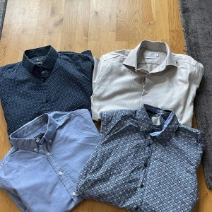 Skjortor i klädpaket mönster - Säljer fyra skjortor i ett paket!  Den ljusblåa saknar en knapp med det finns extraknapp insydd på insidan som man kan sätta dit. Annars är den i bra skick Den vita har 2 mindre fläckar , jag har försökt ta bild på dem men det är lite svårt att se både på bild och i verkligheten.   Den mellan mörka blåa med mönster har en liten röd fläck på ena ärmen, det syns knappt heller och går kanske bort i tvätten.   Den mörkaste skjortan har inga skavanker  skriv för fler bilder!!! Riley, olymp,East west