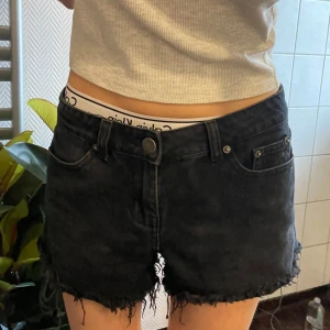 Svarta jeansshorts med fransar - Snygga svarta jeansshorts med fransiga kanter. Perfekta för en avslappnad stil. De har klassisk femficksdesign och knappgylf.