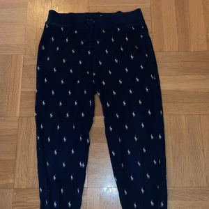 Svarta mjukisbyxor från Ralph Lauren - Säljer ett par svarta mjukisbyxor från Ralph Lauren med ett diskret mönster av små vita logotyper. Byxorna har en bekväm passform med resår i midjan och snörning för justering.